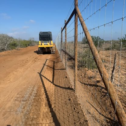 Freshly cut caliche ranch road beside a game fence
